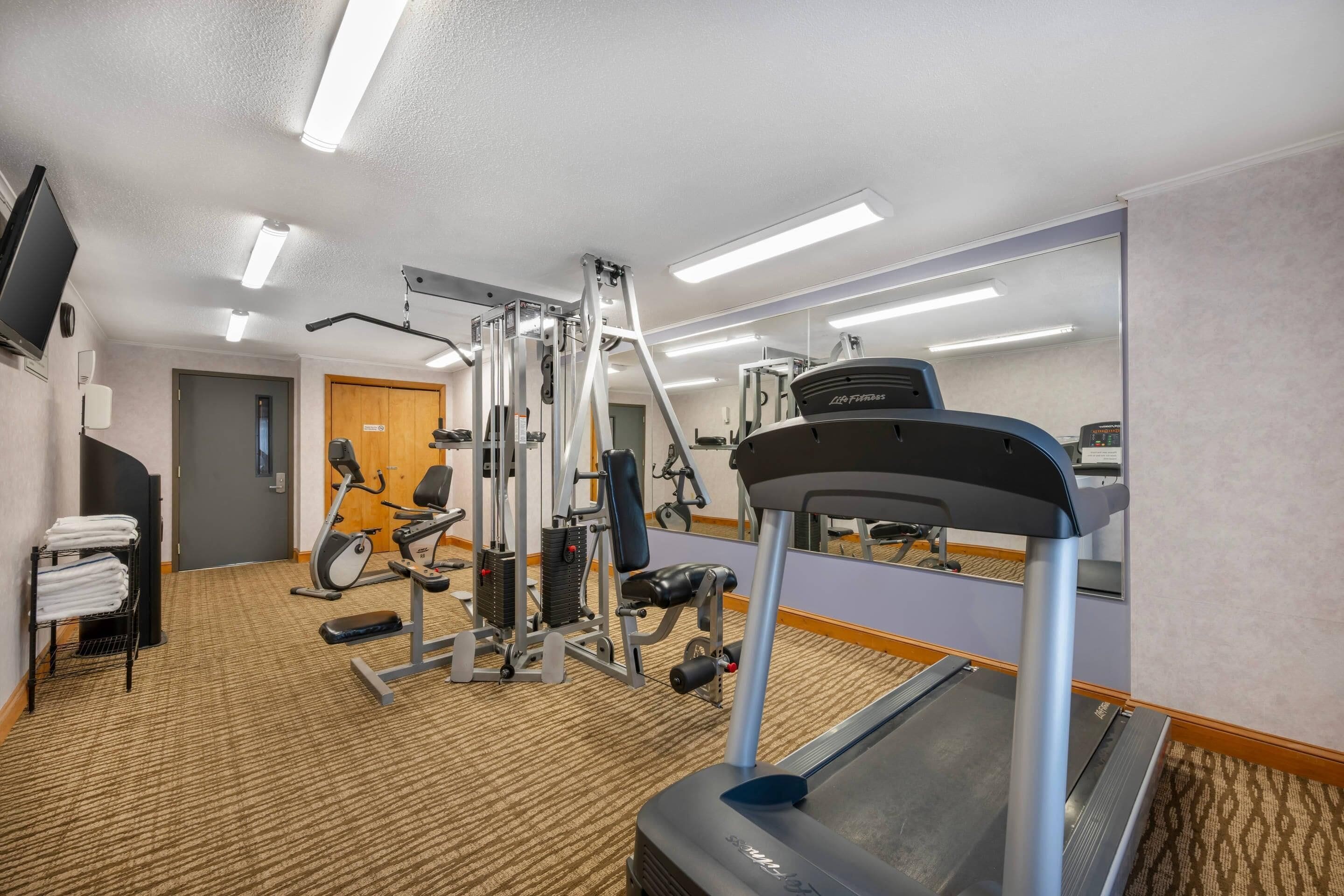 Ein Fitnessraum in einem Hotel mit Cardiogeräten, Krafttrainingsgeräten und einer Spiegelwand.