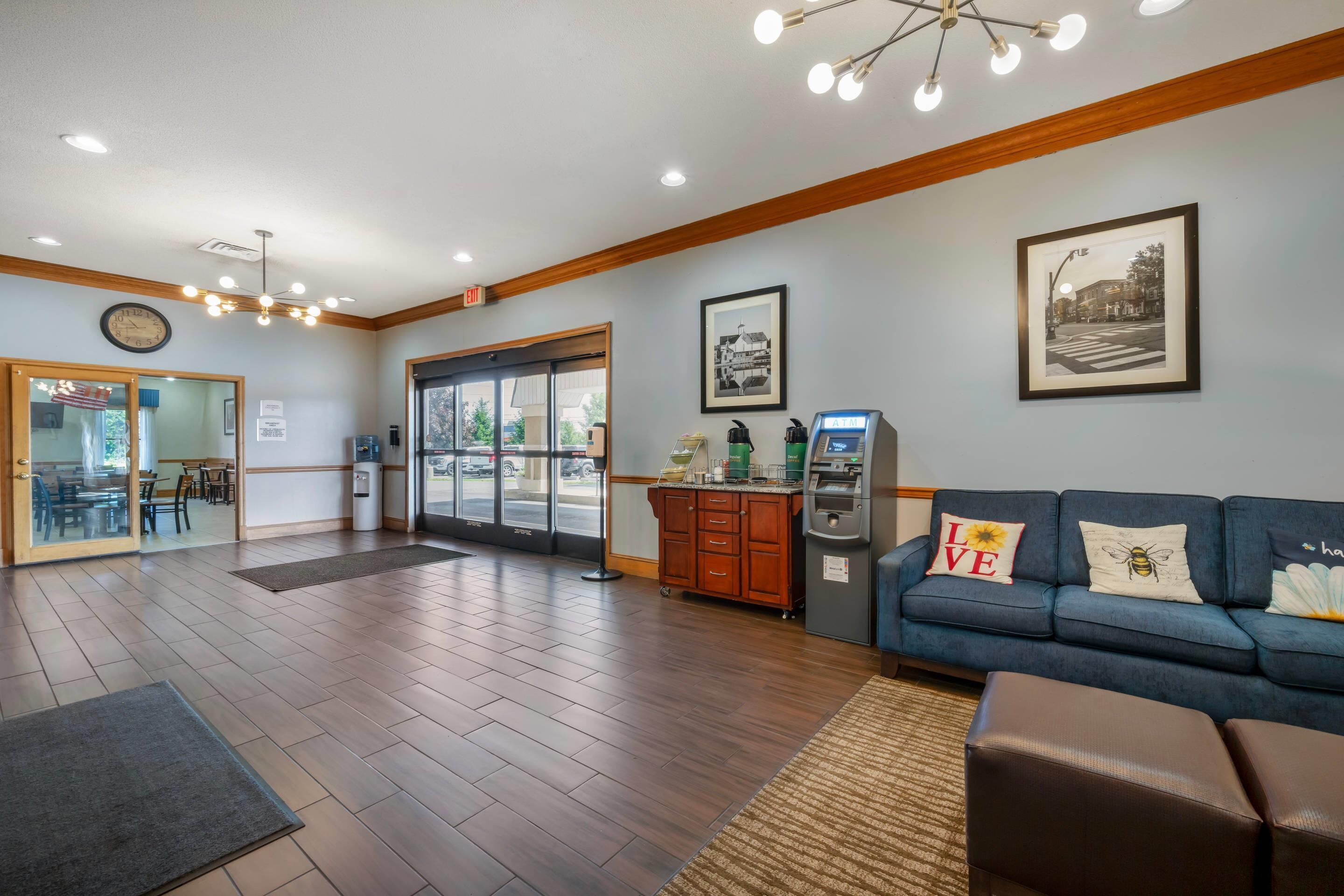 A lobby with a reception desk, a blue sofa with decorative pillows, an ATM, and a framed picture on the wall.