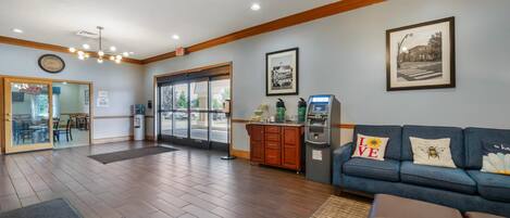 A lobby with a reception desk, a blue sofa with decorative pillows, an ATM, and a framed picture on the wall.