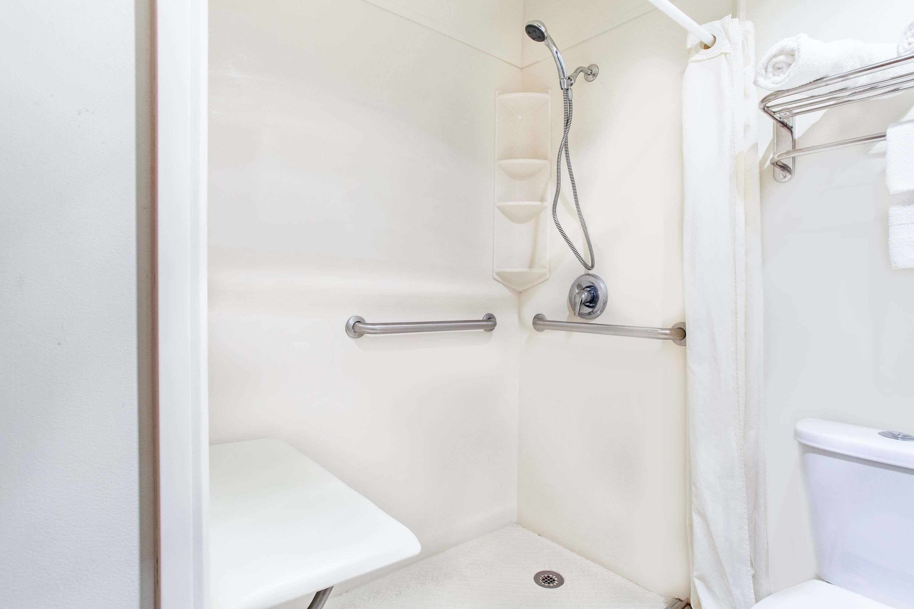A white bathroom with a shower, grab bars, a towel rack, and a toilet.