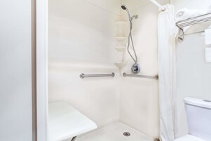 Un baño blanco con ducha, barras de apoyo, toallero y retrete.