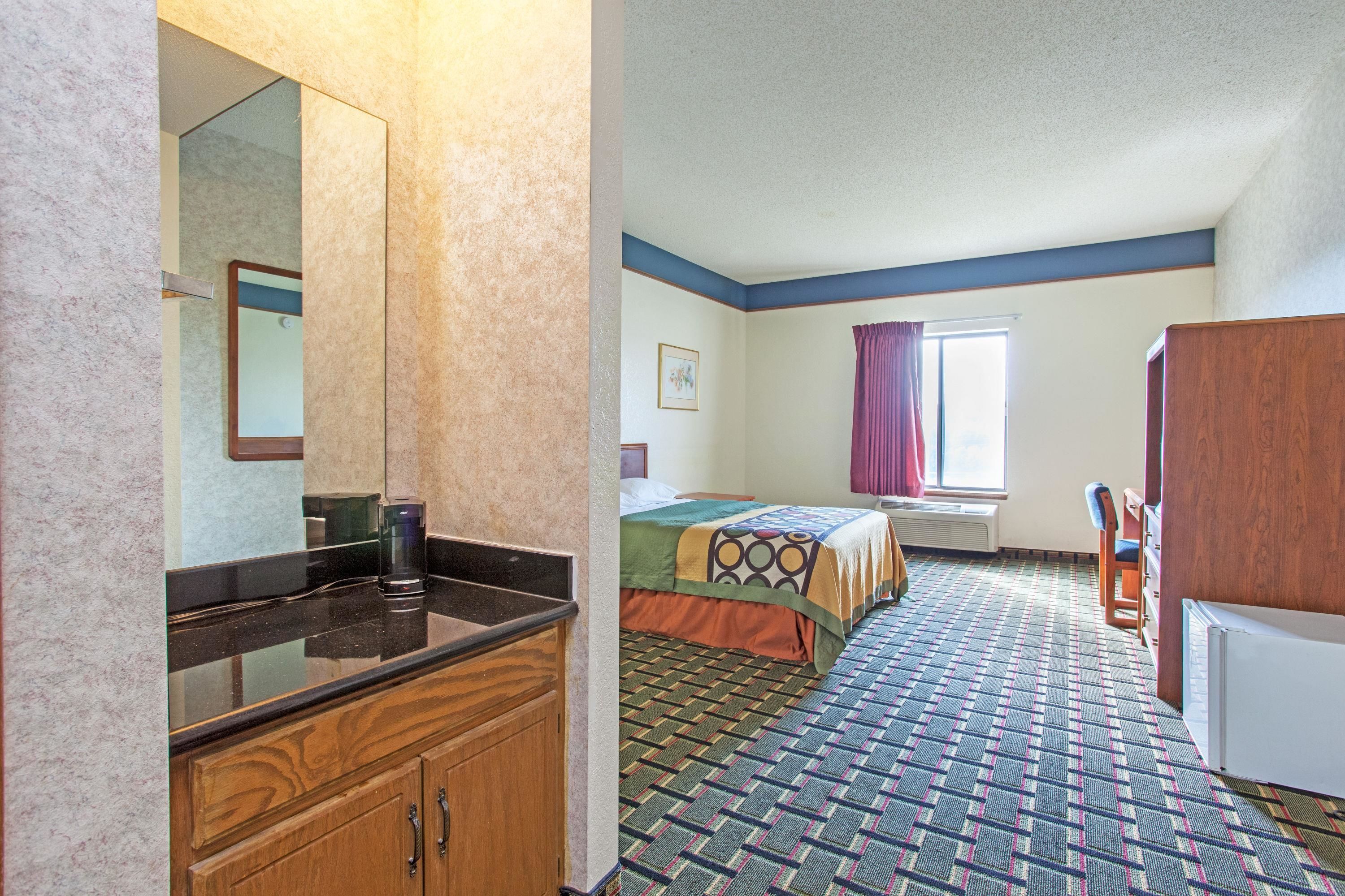A hotel room with a bed, a desk, a chair, a mirror, and a radiator.