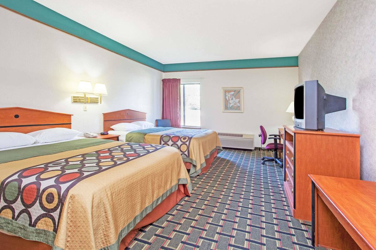 Una habitación de hotel con dos camas, un escritorio, un televisor y una ventana con cortinas.