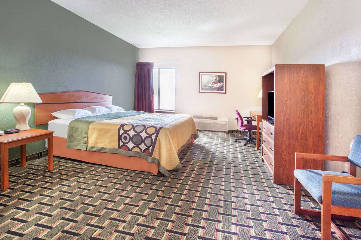 Habitación de hotel con cama, escritorio, silla, televisor y ventana.