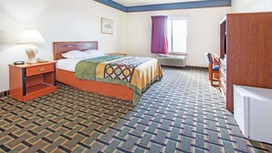 Une chambre d’hôtel comprenant un lit, une table de chevet, un bureau, une chaise, une fenêtre avec des rideaux et un radiateur.