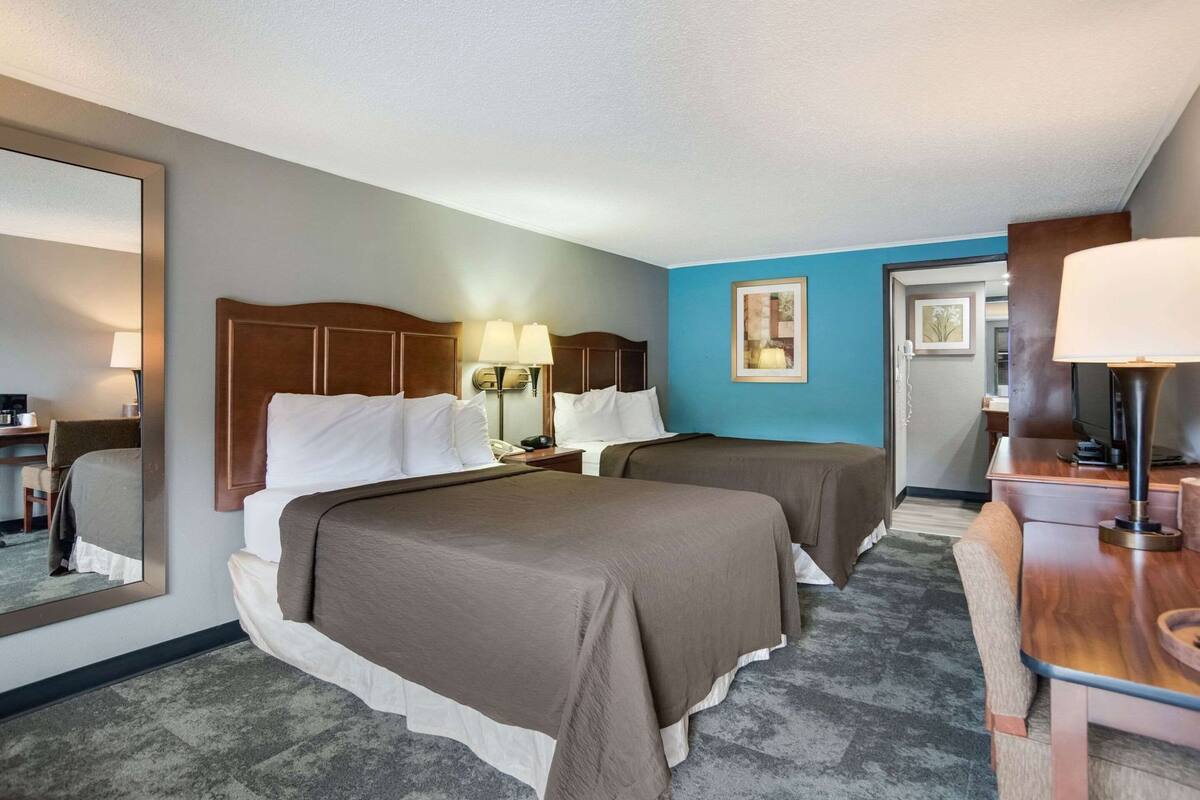 A hotel room with two beds, a desk, a chair, a mirror, and a door.