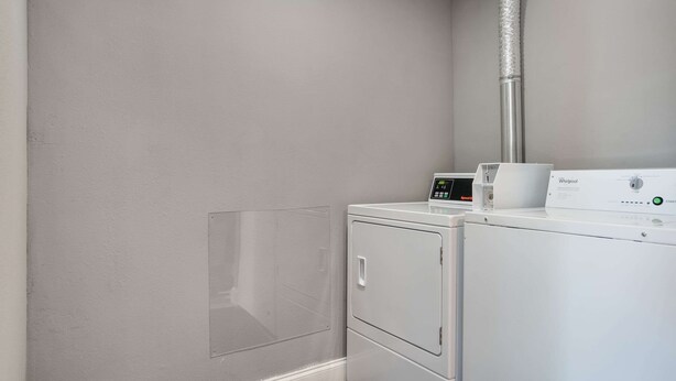 A laundry room with a white washing machine and dryer, a clear plastic window, and a vent pipe on the wall. - Rodeway Inn Carlisle North (Carlisle)
