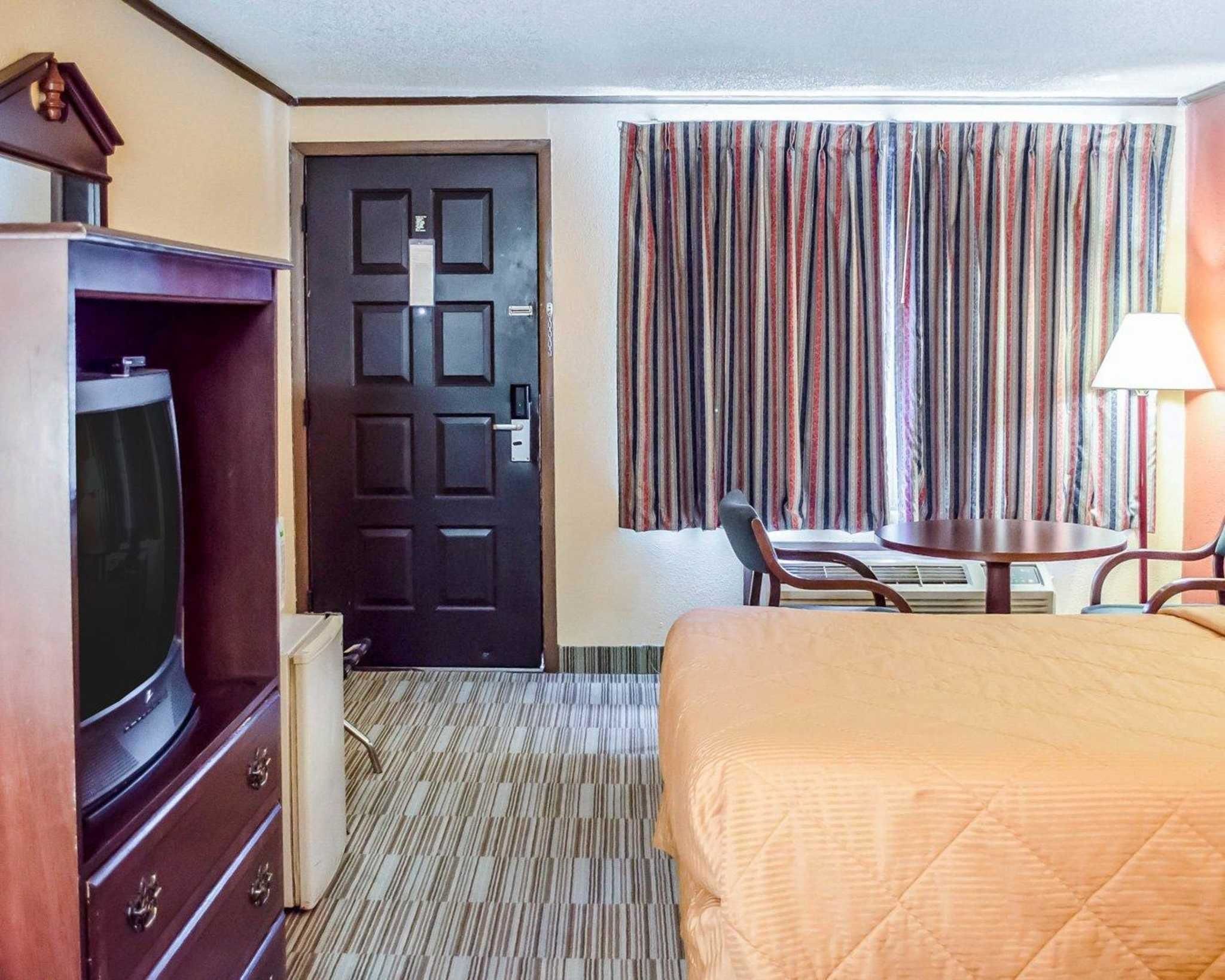 A hotel room with a bed, a TV, a desk with a chair, and a window with curtains.