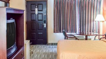 A hotel room with a bed, a TV, a desk with a chair, and a window with curtains.