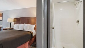 Ett hotellrum med en säng, ett nattduksbord, en lampa och en duschhörna.