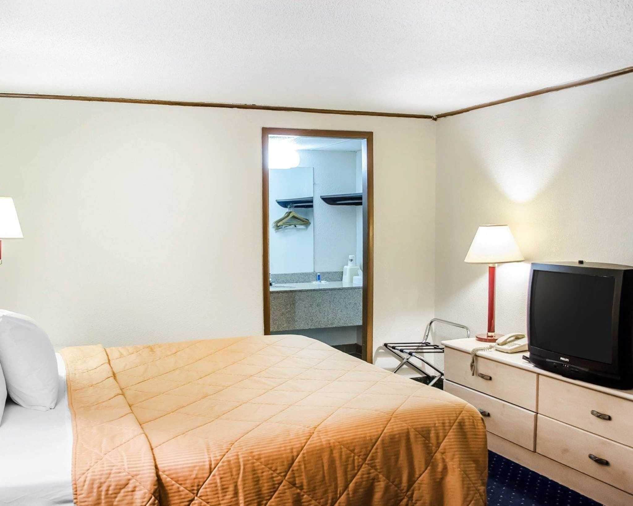 A hotel room with a bed, a TV, a desk with a lamp, and a mirror.