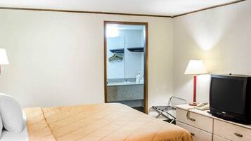 A hotel room with a bed, a TV, a desk with a lamp, and a mirror.