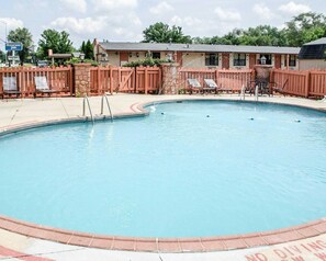 A swimming pool with a wooden fence, lounge chairs, and a building in the background.