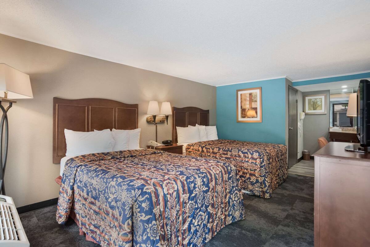 A hotel room with two beds, a desk, a chair, a lamp, and a painting on the wall.