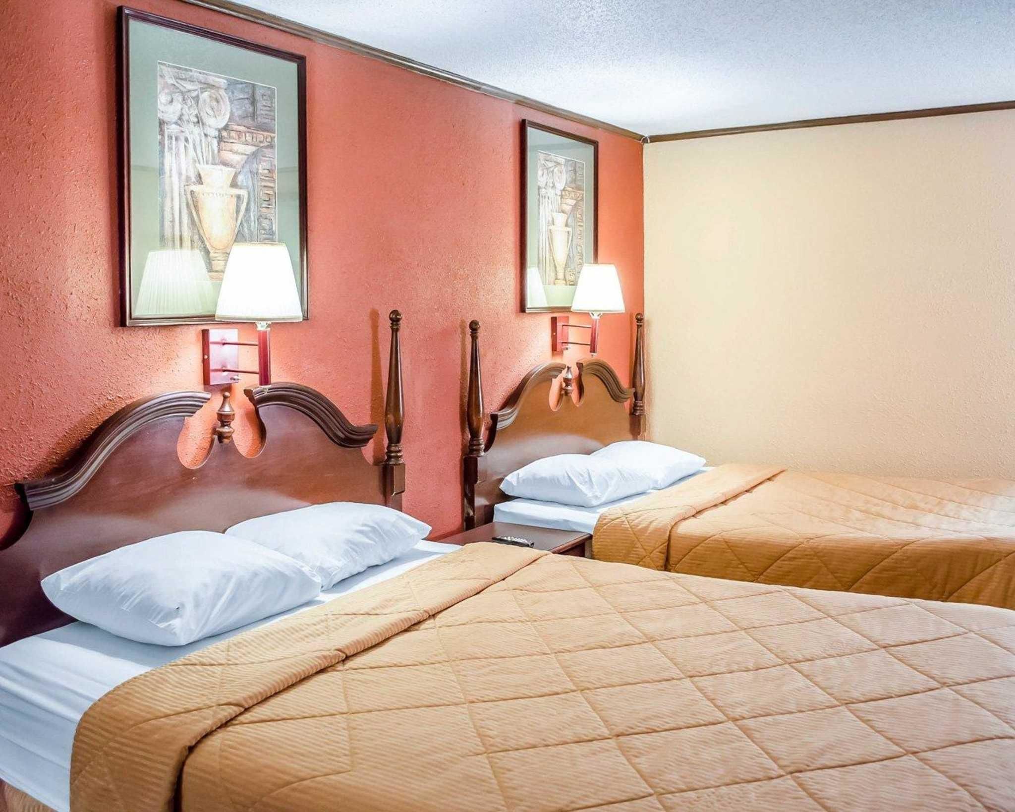 Een hotelkamer met twee bedden, elk voorzien van een houten hoofdbord en witte beddengoed. Aan weerszijden van de bedden hangen twee wandlampen.