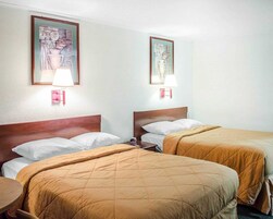 Habitación de hotel con dos camas, cada una con cabecero de madera y ropa de cama blanca. Dos lámparas de pared con abatidores rojos y dos obras de arte enmarcadas sobre las camas.