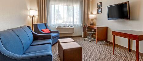 A hotel room with a blue sofa, a desk, a television, and a large window with curtains.
