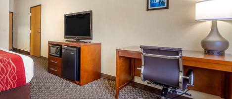 A hotel room with a bed, a desk with a computer, a television, a lamp, and a microwave.