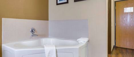 Un baño con una bañera grande, azulejos blancos y dos cuadros en la pared.