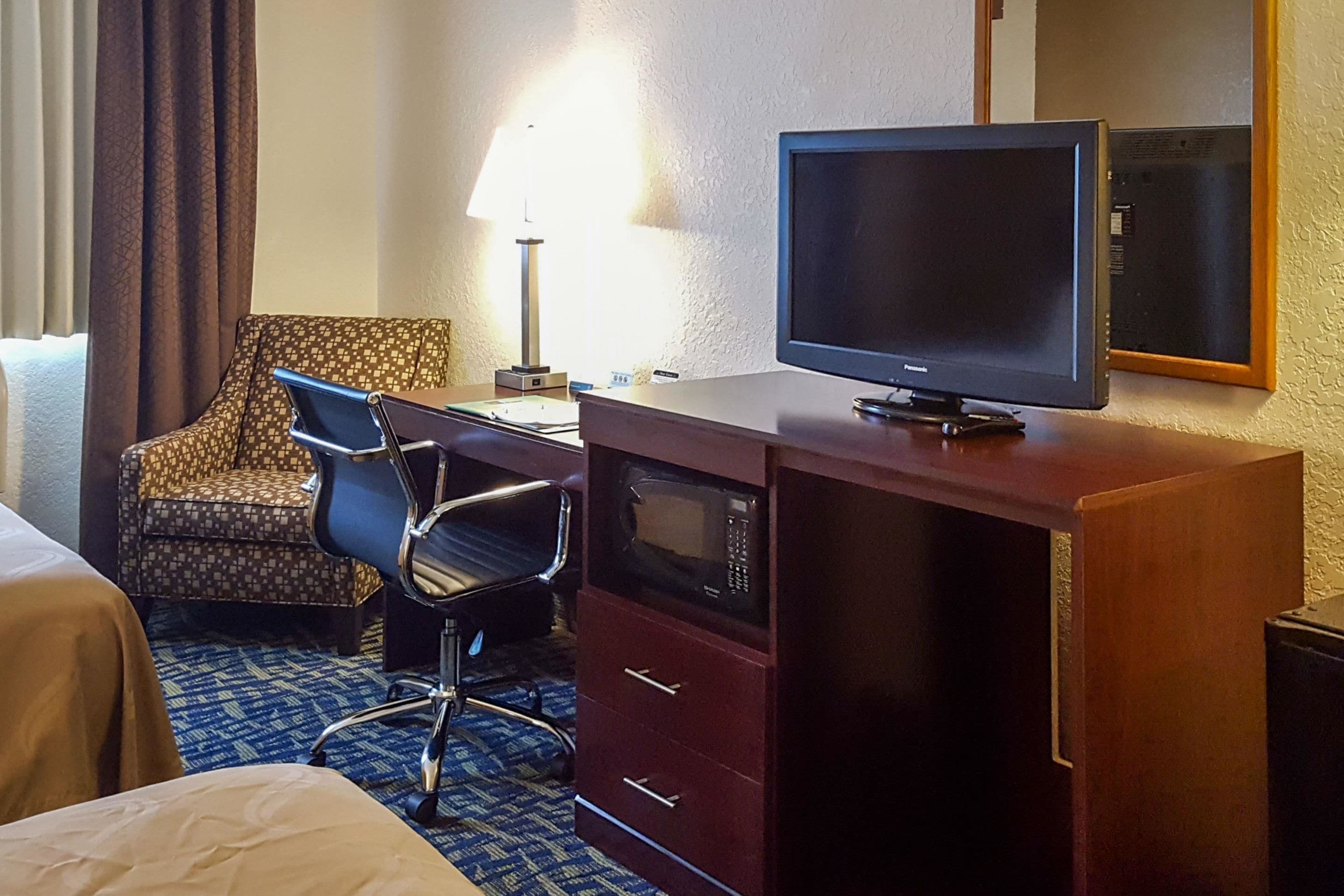 A hotel room with a bed, a desk with a television, a microwave, and a chair.