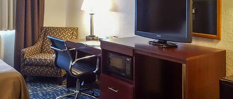 A hotel room with a bed, a desk with a television, a microwave, and a chair.