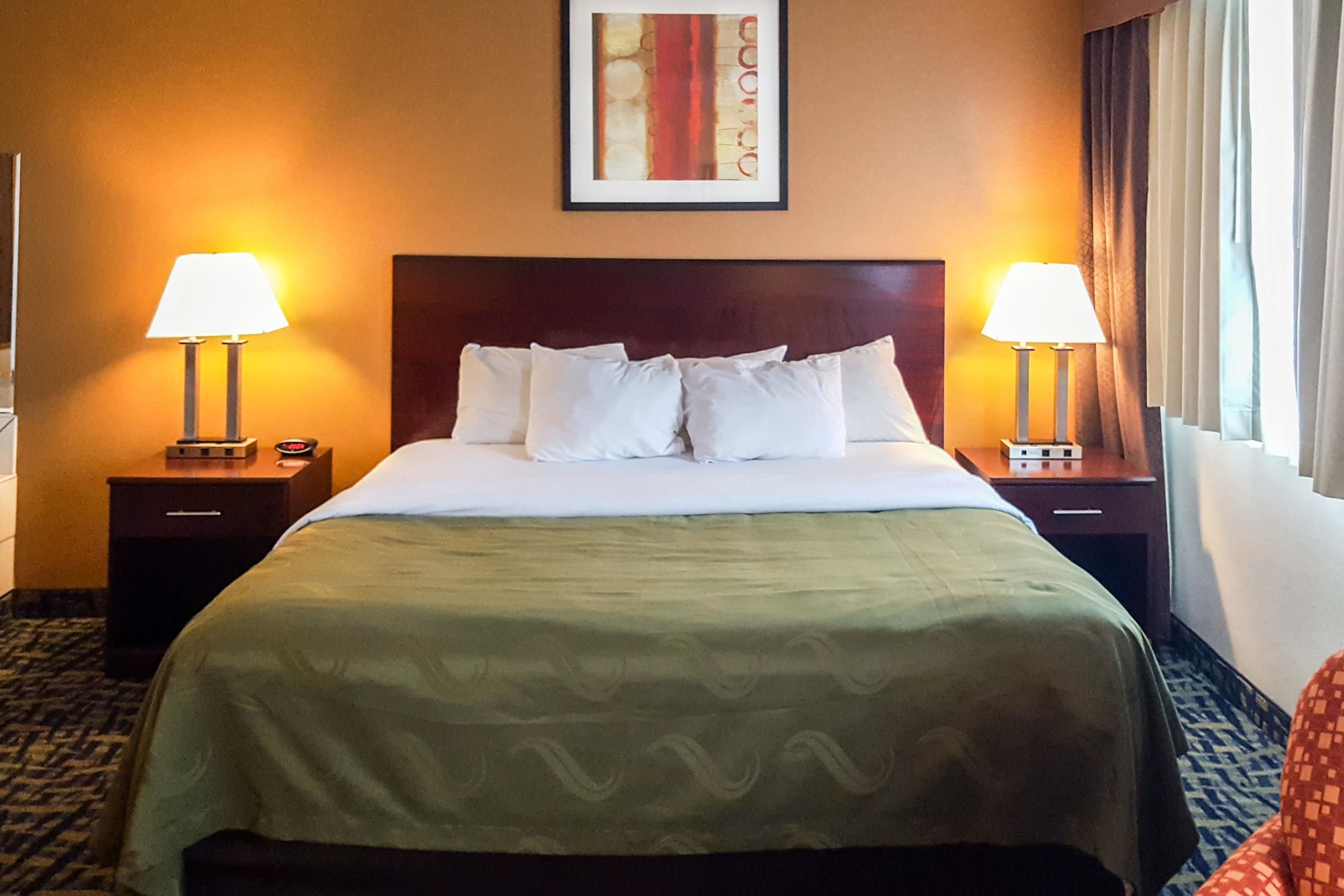 A hotel room with a large bed, two bedside tables with lamps, a framed picture on the wall, and a window with curtains.