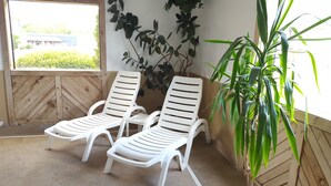 Two white plastic lounge chairs in a sunroom with a wooden floor, a large window, and a potted plant. - Quality Inn Ozark-Springfield South (Ozark)