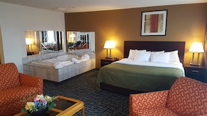 A hotel room with a large bed, two armchairs, a sofa, a small table with a vase of flowers, a bathtub, and a large mirror. - Quality Inn Ozark-Springfield South (Ozark)