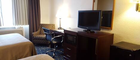 Een hotelkamer met twee bedden, een bureau met een televisie, een stoel, een bureaulamp en een magnetron.