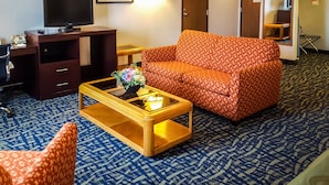 A hotel room with a sofa, a coffee table with a flower vase, a TV on a wooden cabinet, and a patterned carpet. - Quality Inn Ozark-Springfield South (Ozark)