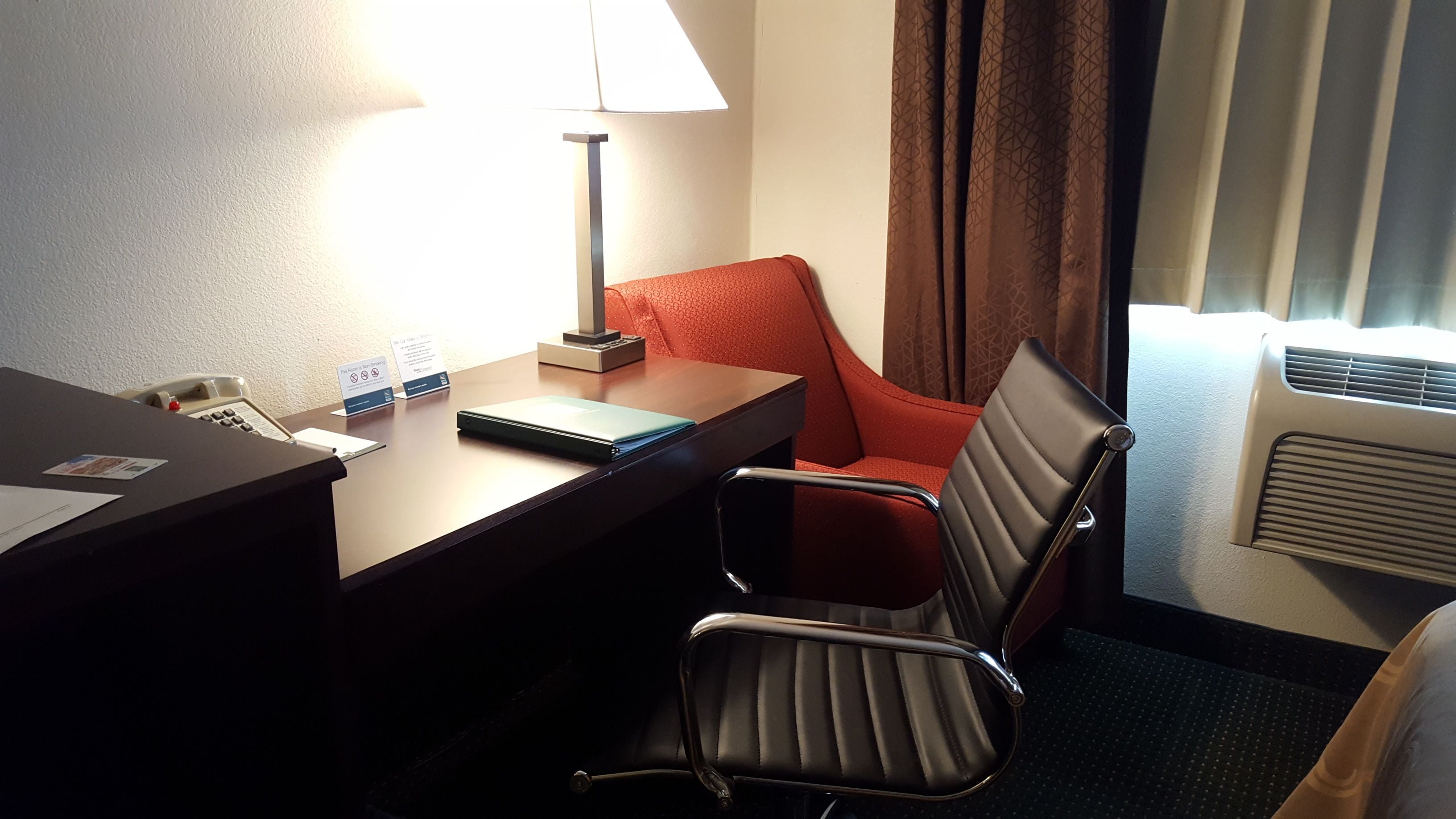 Une chambre d’hôtel équipée d’un bureau, d’une chaise, d’une lampe, d’un téléphone et d’une fenêtre avec des rideaux.