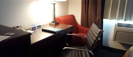 Une chambre d’hôtel équipée d’un bureau, d’une chaise, d’une lampe, d’un téléphone et d’une fenêtre avec des rideaux.