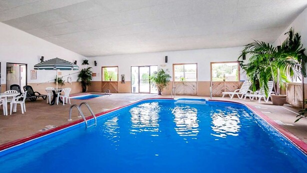 An indoor swimming pool with clear blue water, surrounded by white lounge chairs and tables. - Quality Inn Ozark-Springfield South (Ozark)