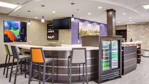 A modern bar area with a curved counter, bar stools, a large TV, and a refrigerator stocked with beverages. - Clarion Pointe Biltmore Village (Asheville)