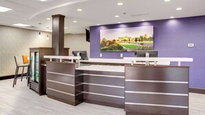A reception area with a counter, chairs, a refrigerator, and a large screen displaying a scenic landscape. - Clarion Pointe Biltmore Village (Asheville)