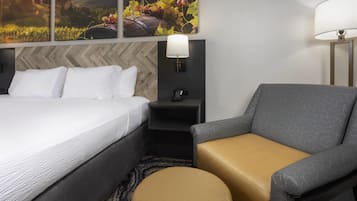 Habitación de hotel con cama, mesita de noche, lámpara, silla y alfombra.