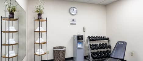 Ett gym med en vattenautomat, hantlar, en bänk och en papperskorg.