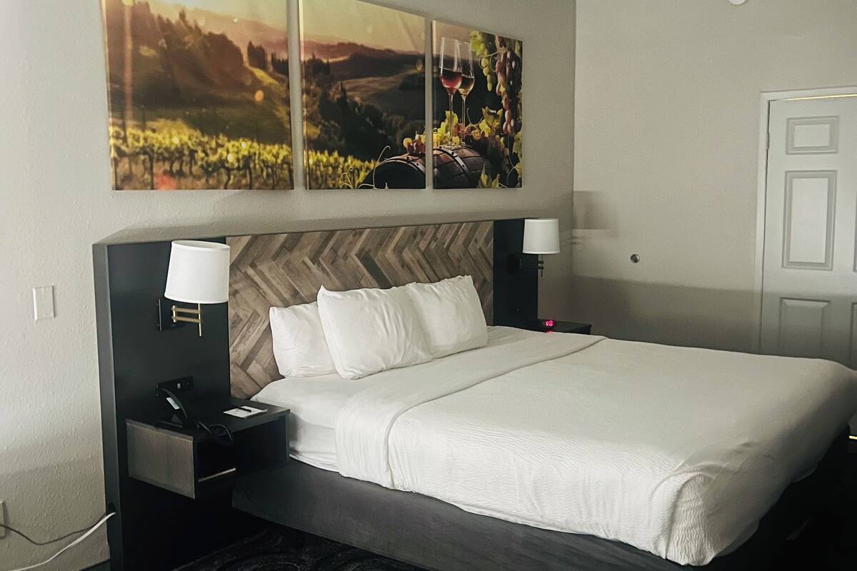 Une chambre d’hôtel avec un lit, des tables de chevet, une lampe, une chaise et un grand tableau au-dessus du lit.