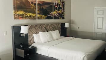 A hotel room with a bed, bedside tables, a lamp, a chair, and a large painting above the bed.