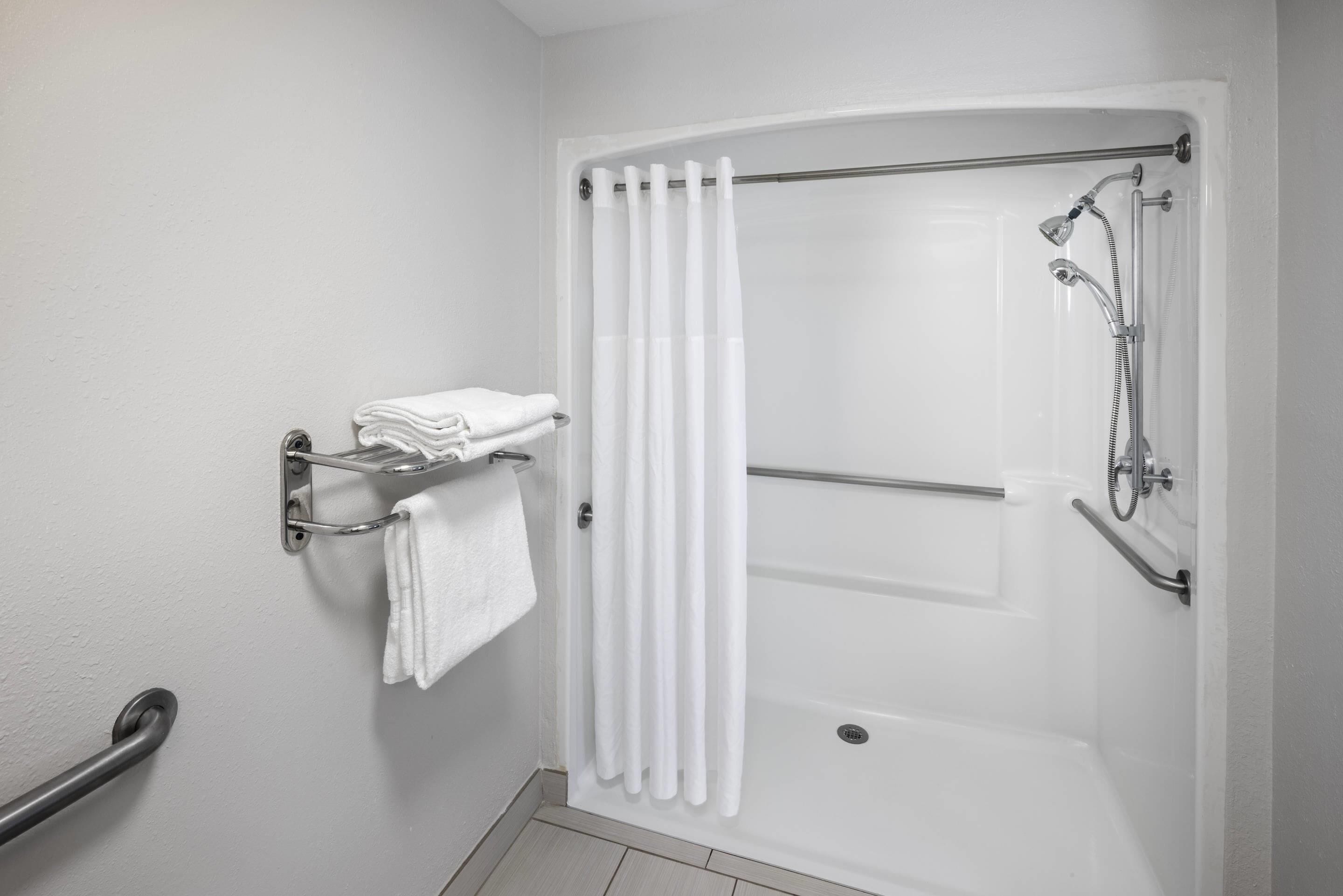 A modern bathroom with a walk-in shower, a towel rack with folded towels, and a grab bar for safety.
