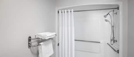 Ein modernes Badezimmer mit bodenebener Dusche, einem Handtuchhalter mit gefalteten Handtüchern und einer Haltestange zur Sicherung.