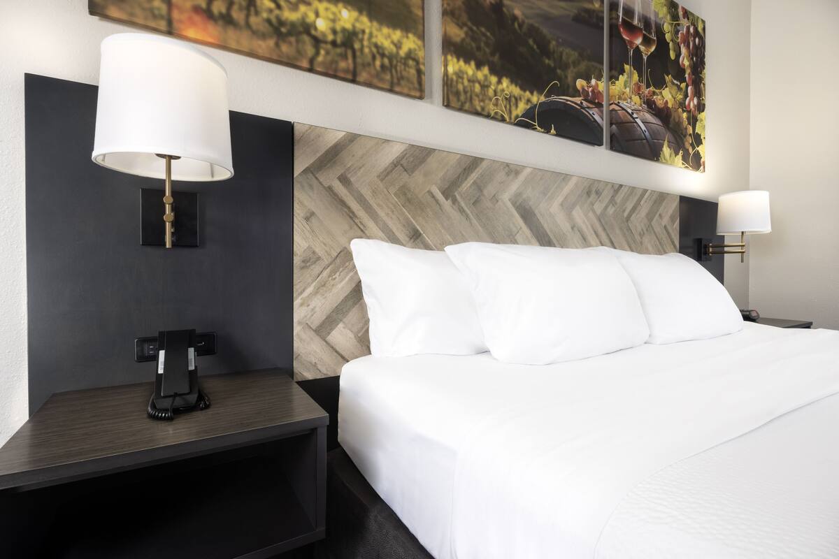 Une chambre d’hôtel avec un grand lit, deux tables de chevet, une lampe moderne et des œuvres d’art accrochées au mur.