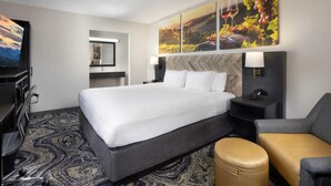A hotel room with a large bed, a desk with a chair, a small table, a sofa, and a wall-mounted TV. - Clarion Pointe Biltmore Village (Asheville)