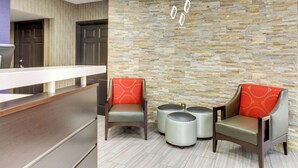 A reception area with a stone wall, two armchairs with red cushions, and a counter. - Clarion Pointe Biltmore Village (Asheville)