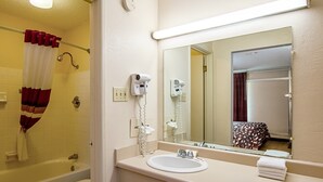 A bathroom with a bathtub, a sink, a hairdryer, and a mirror. - Red Roof Inn Battle Creek (Battle Creek)