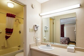 A bathroom with a bathtub, a sink, a hairdryer, and a mirror. - Red Roof Inn Battle Creek (Battle Creek)