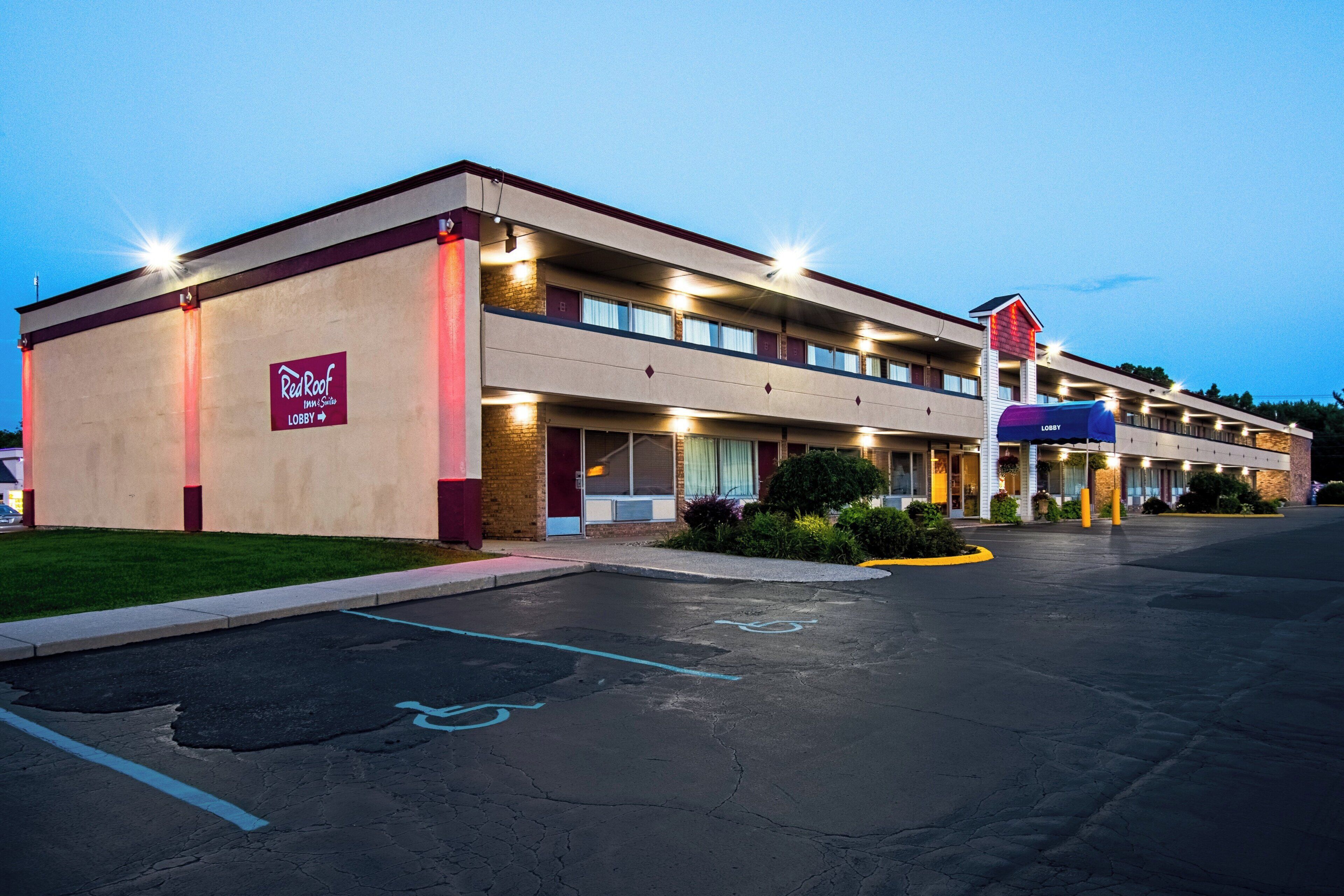 A Red Roof Inn & Suites with a two-story building, a covered parking area, and a clear sky.