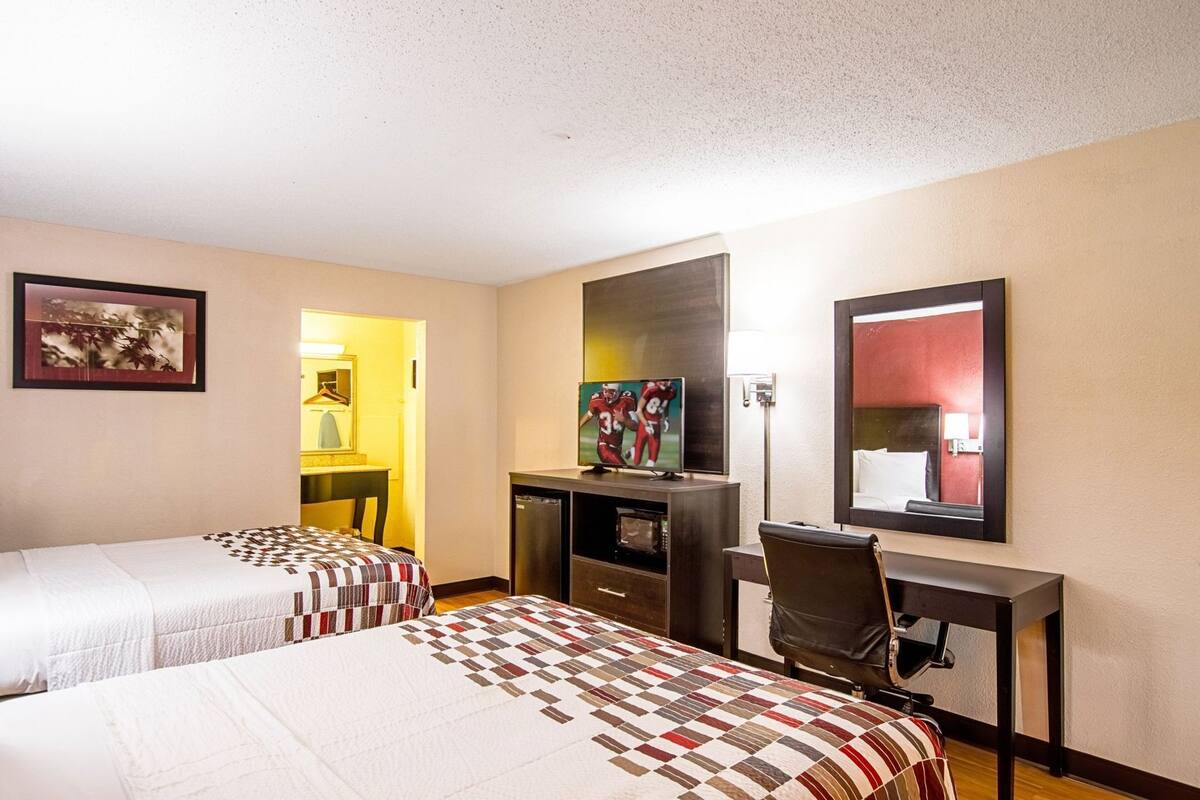 A hotel room with two beds, a desk, a chair, a television, and a mirror.