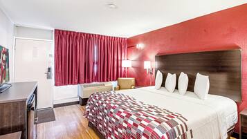 A hotel room with a bed, a desk, a chair, a TV, and a red curtain.