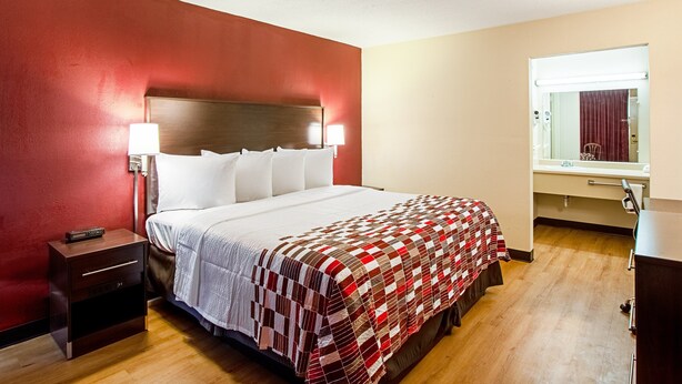 A hotel room with a bed, nightstand, and a mirror. - Red Roof Inn Battle Creek (Battle Creek)
